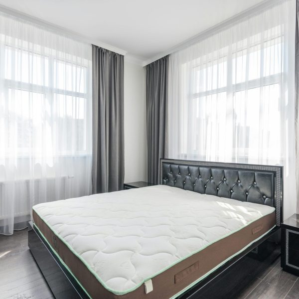 A bright and modern bedroom with a stylish bed, sheer curtains, and minimal decor.